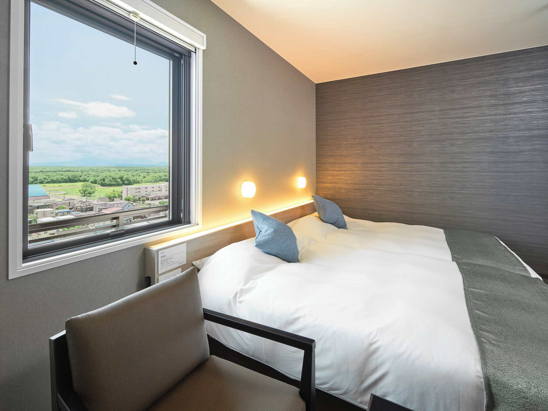A hotel room with a bed, a desk, and a window with a city view.