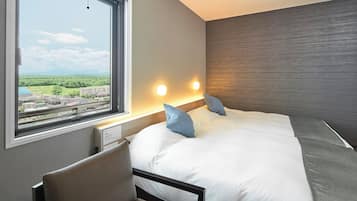 A hotel room with a bed, a desk, and a window with a city view.