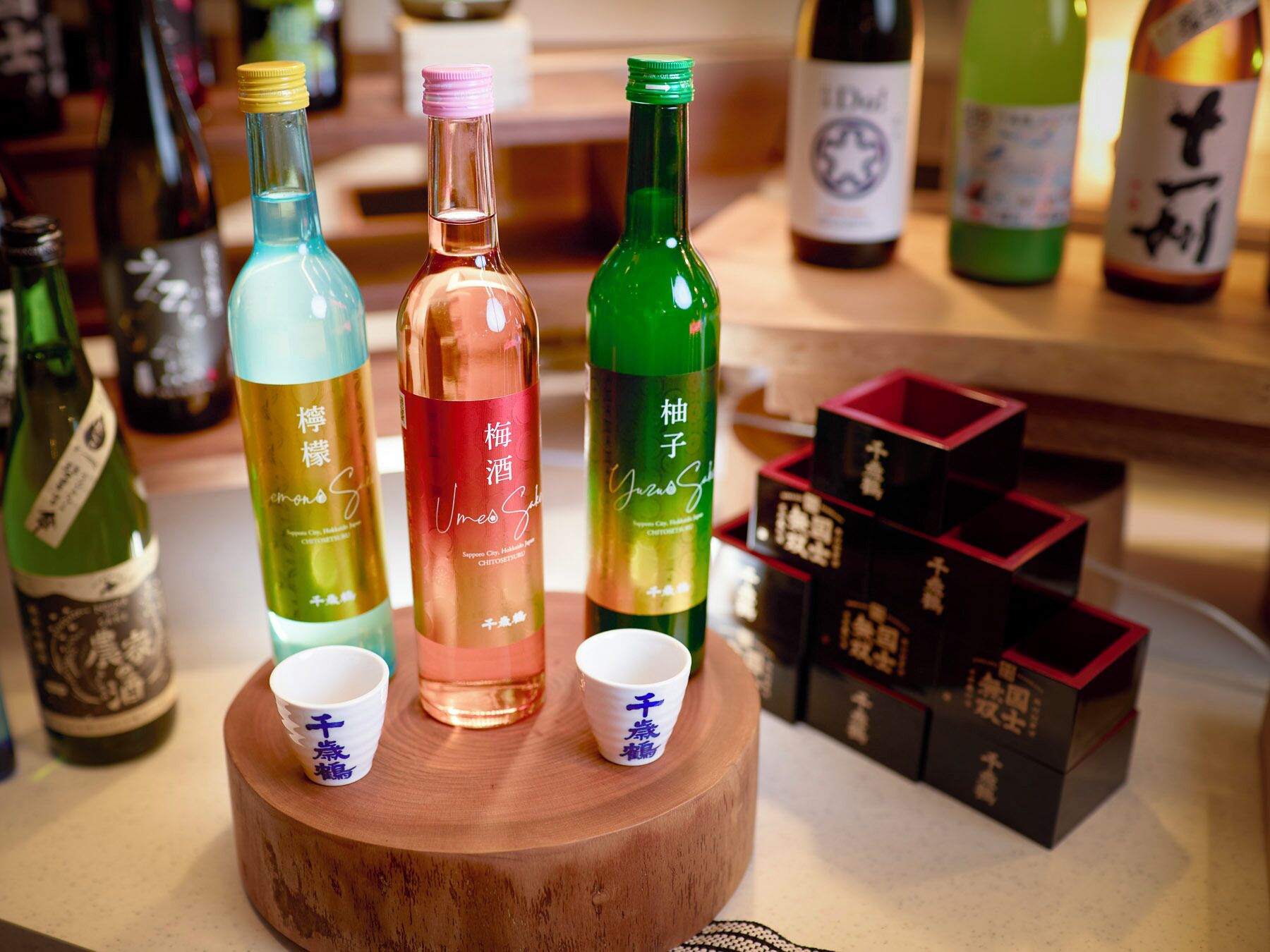 A selection of bottles on a wooden stand with two small cups.