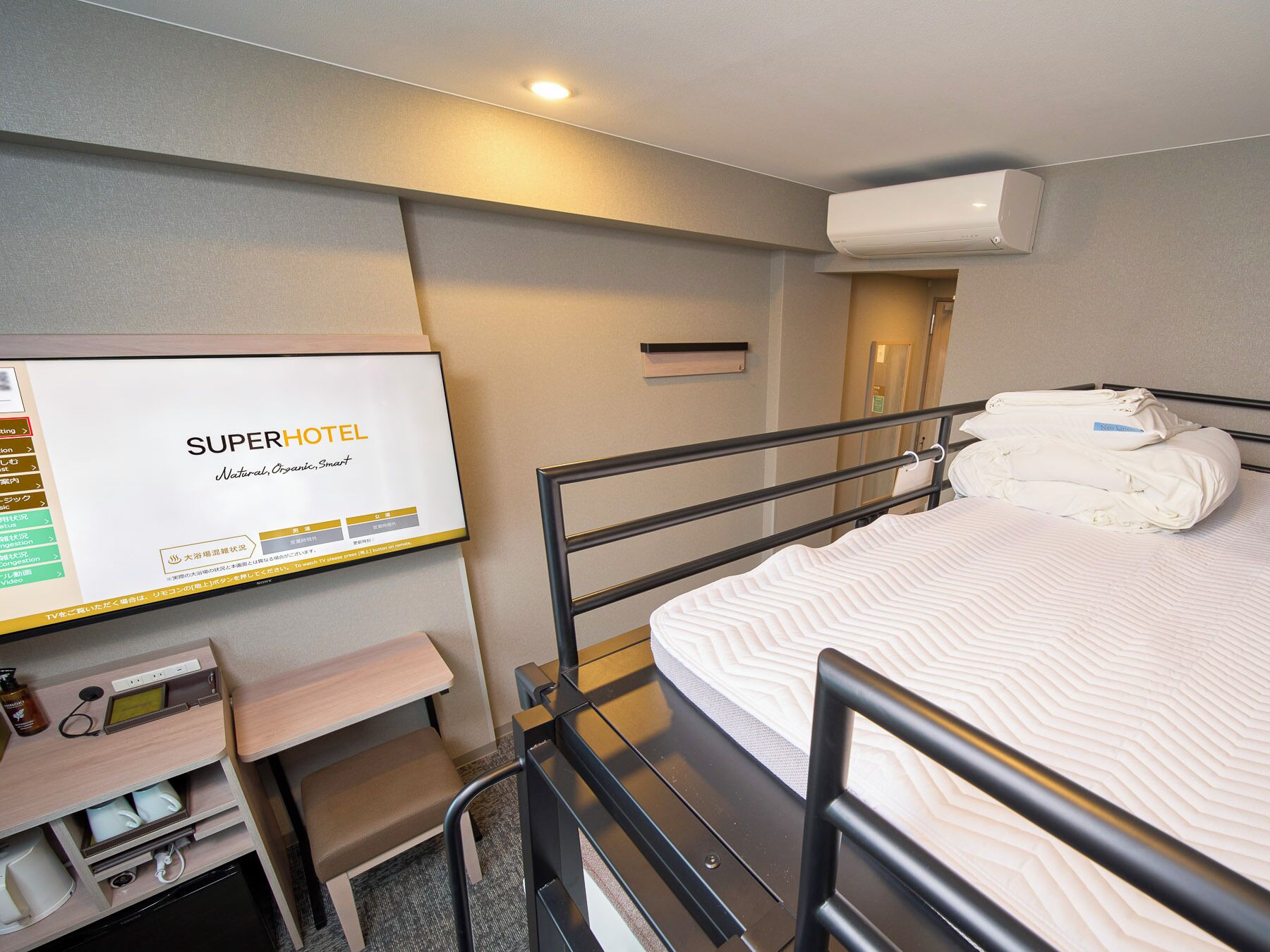 A hotel room with a bunk bed, a desk with a computer, and a TV displaying hotel information.