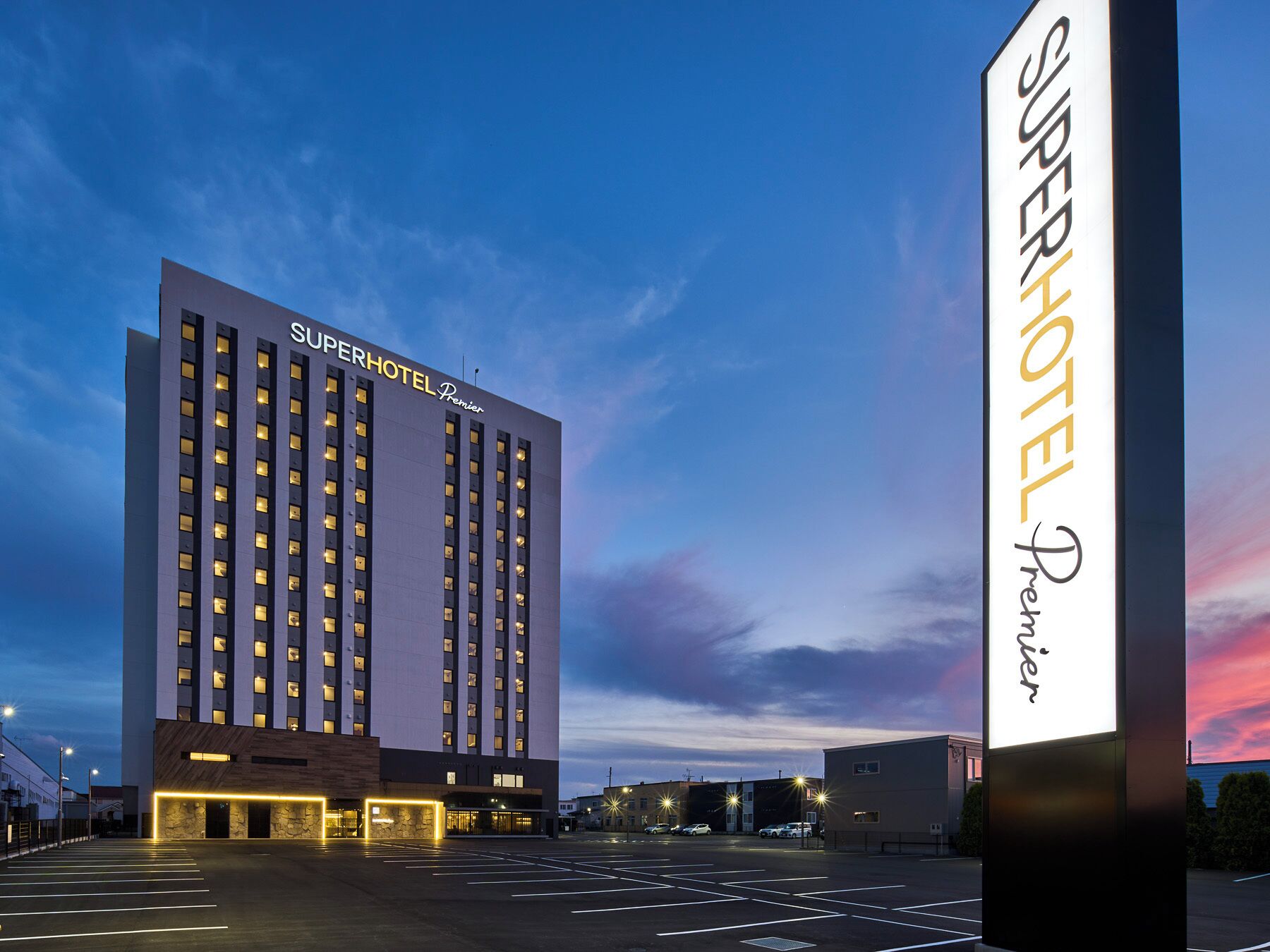 Ein SuperHotel Premier Gebäude mit modernem Design, mehreren Etagen und einer gut beleuchteten Fassade.
