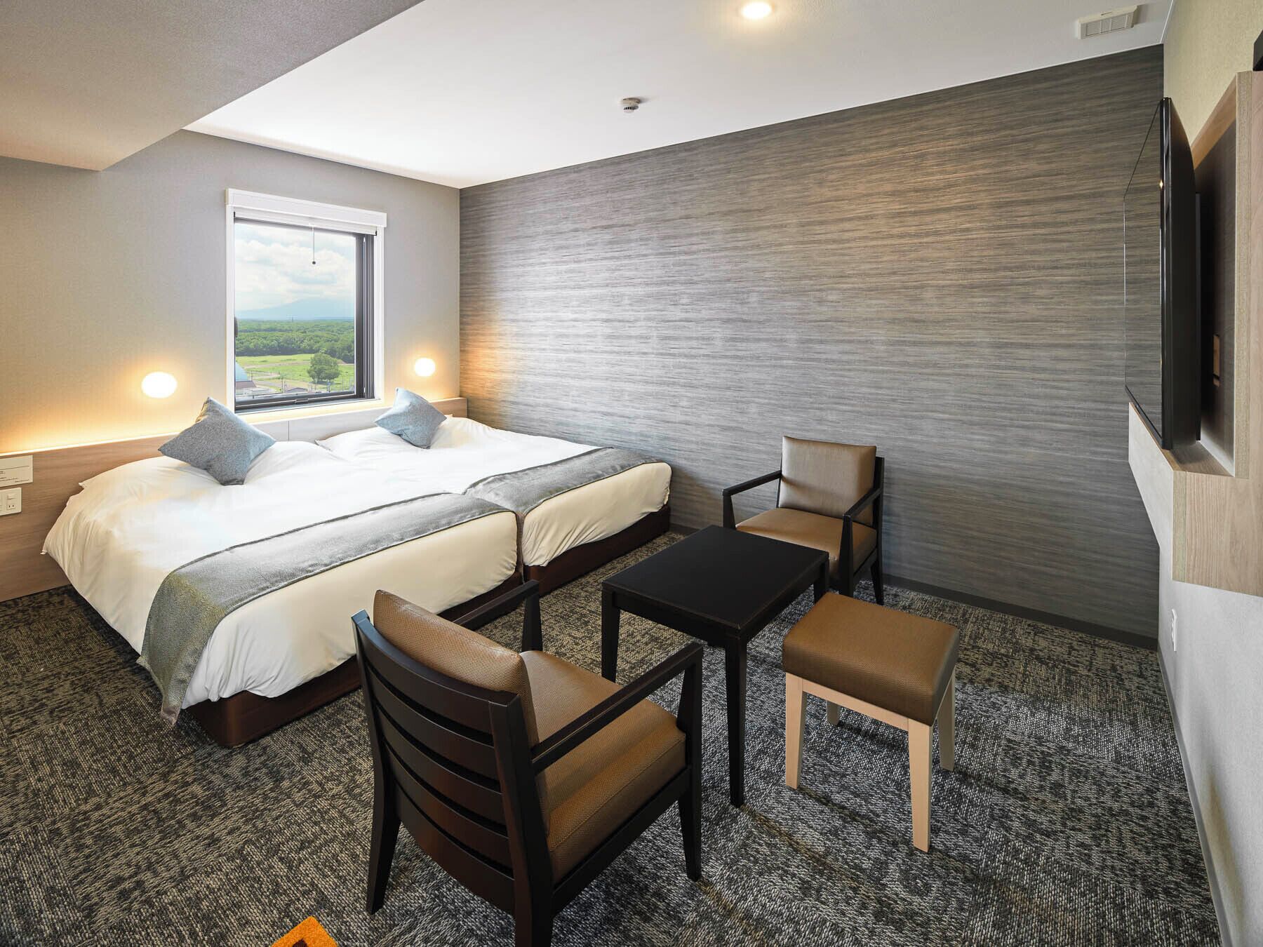 A hotel room with a bed, two chairs, a table, and a TV.