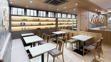 Un interno ristorante moderno con lunghi tavoli comuni, sedie in legno e una mensola a parete che espone diversi oggetti.