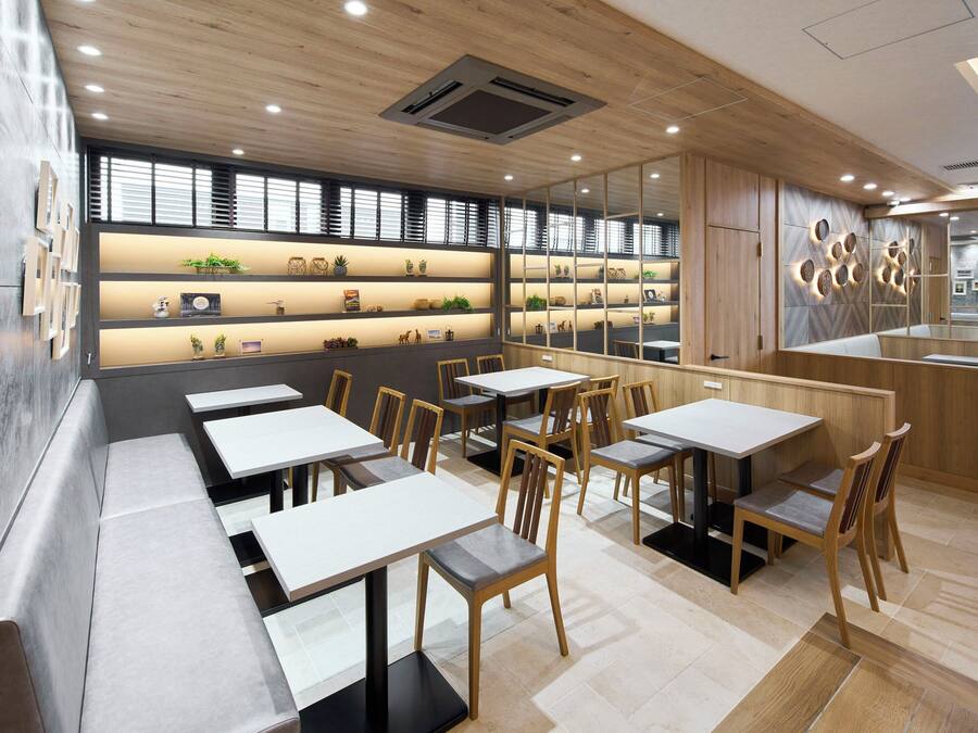 Un interno ristorante moderno con lunghi tavoli comuni, sedie in legno e una mensola a parete che espone diversi oggetti.