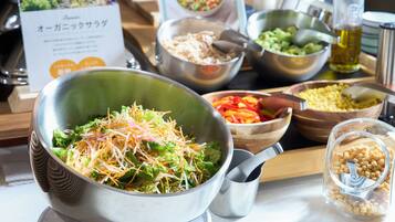 A buffet table with various dishes, including a salad with shredded cheese, bowls of vegetables, and a container of corn.