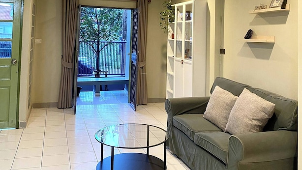 Una sala de estar con un sofá verde, una mesa de centro de vidrio, un armario blanco y vistas a un área exterior a través de una puerta de vidrio.