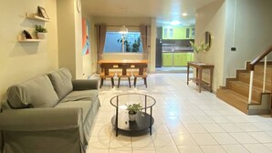 Una sala de estar con sofá, una mesa de centro, una mesa de comedor y una escalera que lleva a una cocina.