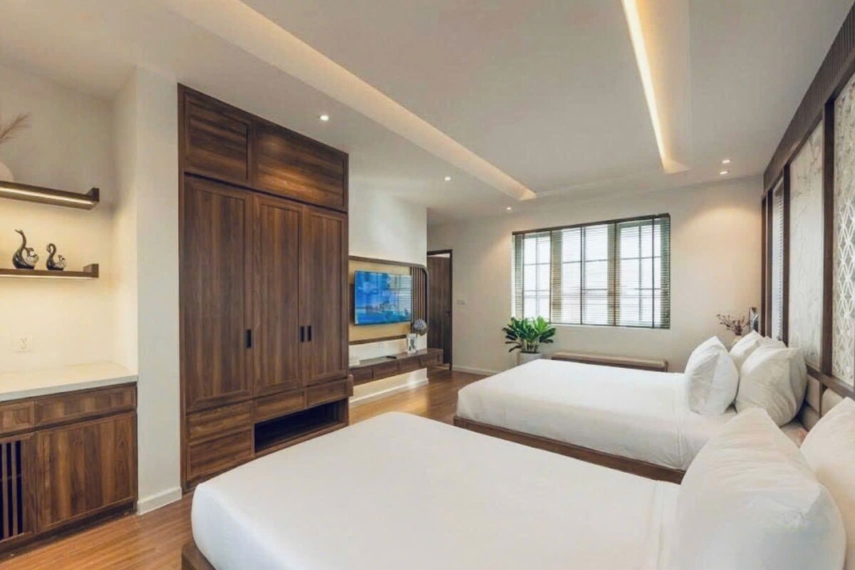 A hotel room with two beds, a large wardrobe, a flat-screen TV, and a window with blinds.