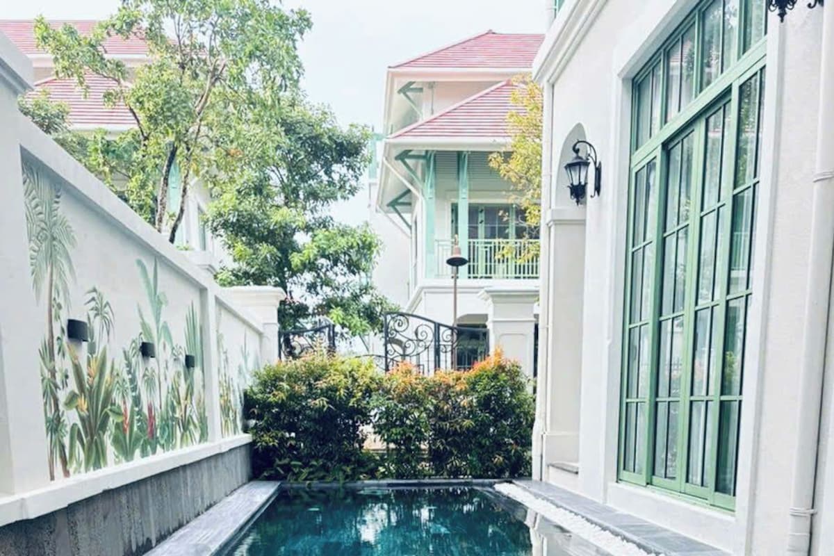 A swimming pool with a clear water surface, surrounded by a low wall and a building with large windows.