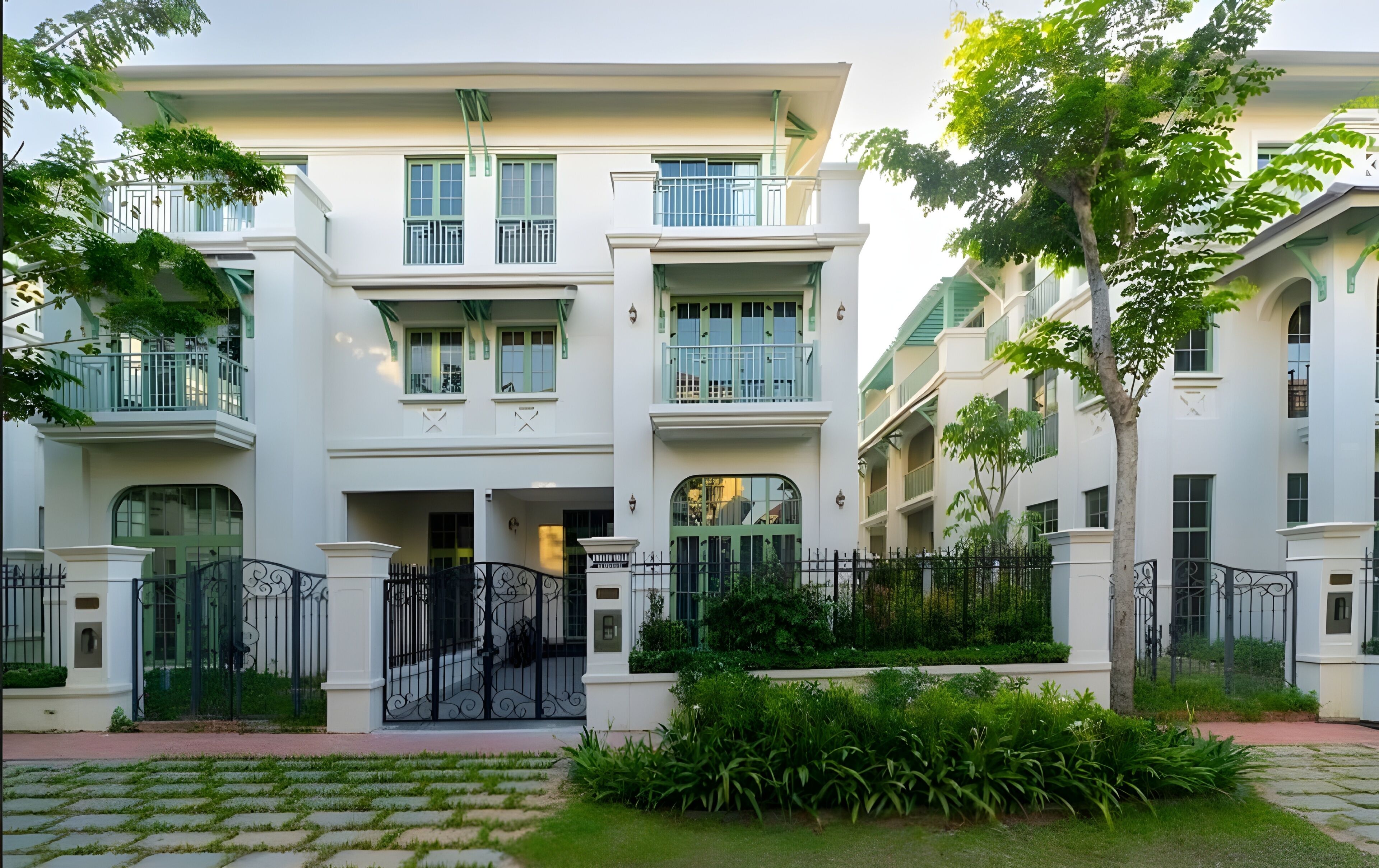 A multi-story building with balconies, a gated entrance, and surrounding greenery.