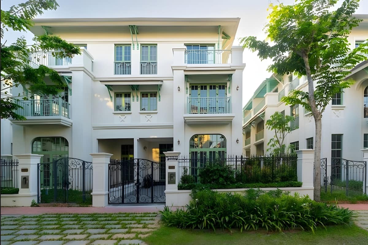 A multi-story building with balconies, a gated entrance, and surrounding greenery.