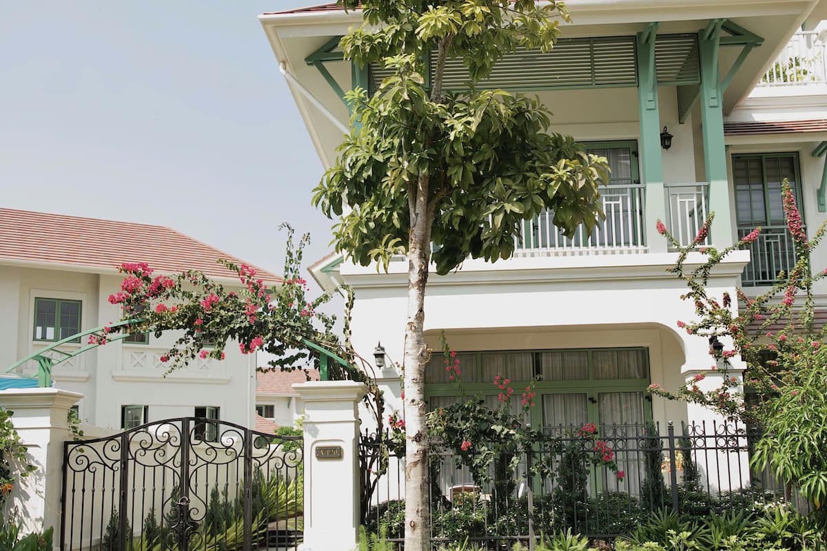 A two-story building with a balcony, a gated entrance, and a tree in the foreground.