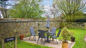 Eine Terrasse mit Tisch und Stühlen, ein Schild für Gäste-Parkplätze und eine Steinmauer.
