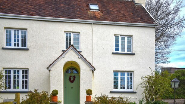 Ein zweistöckiges Haus mit grüner Tür, weißen Fenstern und einer Steintreppe, die zum Eingang führt.