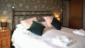 Ein ordentlich bezogenes Bett mit Kissen, einer Nachttischlampe und gefalteten Handtüchern auf einem Nachttisch aus Holz.