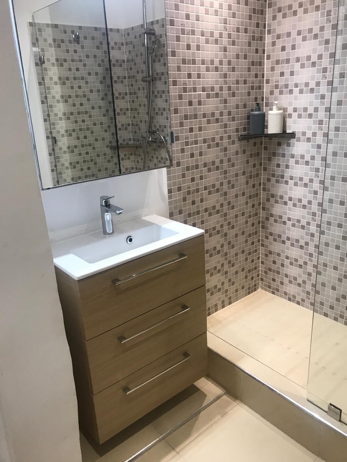 A bathroom with a tiled shower, a sink with a mirror, and a shelf with toiletries.