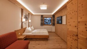 A bedroom with a wooden floor, a bed, a red sofa, a TV, and a window with a view. - Haus Alpenkönig  (Neustift Im Stubaital)
