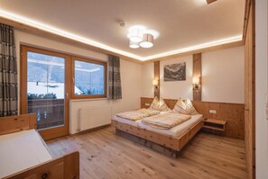 A bedroom with a wooden bed, a window with a view, and a ceiling light fixture. - Haus Alpenkönig  (Neustift Im Stubaital)
