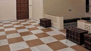 Une pièce spacieuse avec un sol à carreaux, un ventilateur de plafond, une porte et un coin salon avec des coussins.