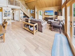 Ein geräumiger Holzraum mit Essbereich, Sofas, einer Treppe und einem großen Fenster mit Blick.