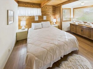 Ein Schlafzimmer mit einem großen Bett, Holzwänden, einem Nachttisch, einer Kommode und einem Fenster.