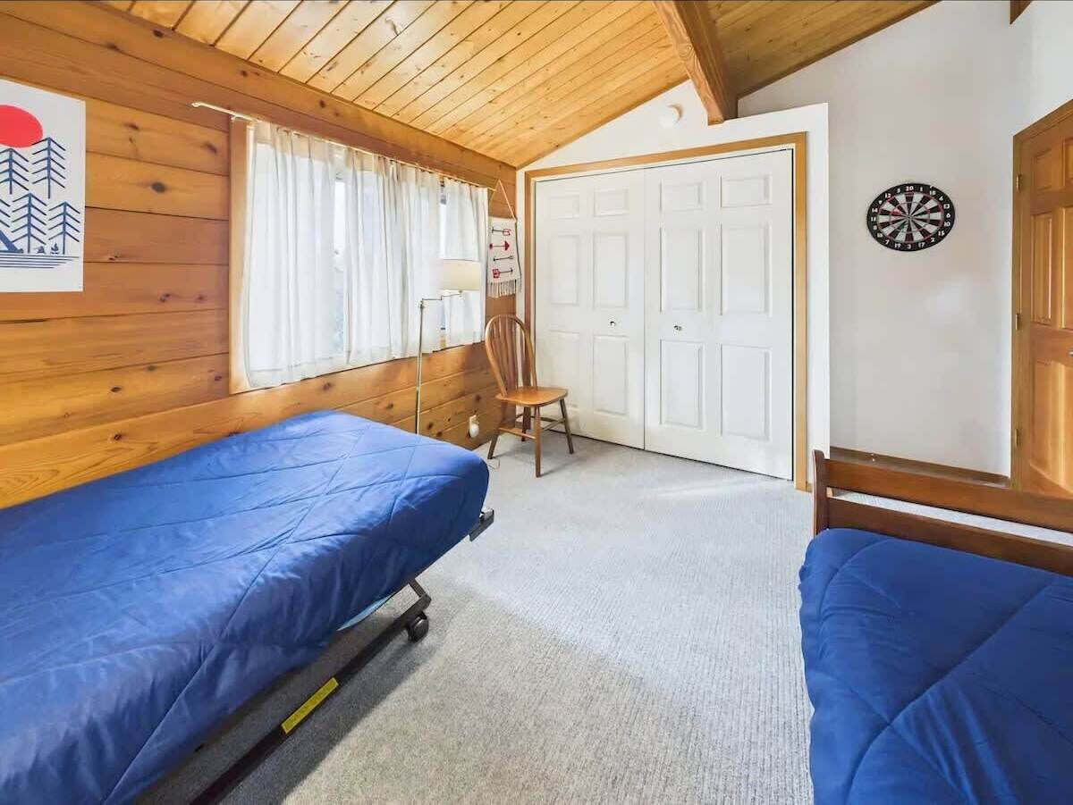 Una habitación con dos camas, una silla, una puerta y un dardo.