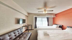 Hotellihuone, jossa on sohva, kaksi sänkyä, televisio, työpöytä ja ilmastointilaite.