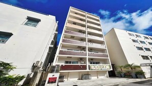 A multi-story building with a sign reading 'CUORE' on the ground floor, air conditioning units, and a parking area with a car. - Hotel Cuore Kokusai Dori Naha (Naha)
