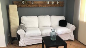 En hvid sofa, et sort bord og en træhylde med dekorative genstande i et hjørne.