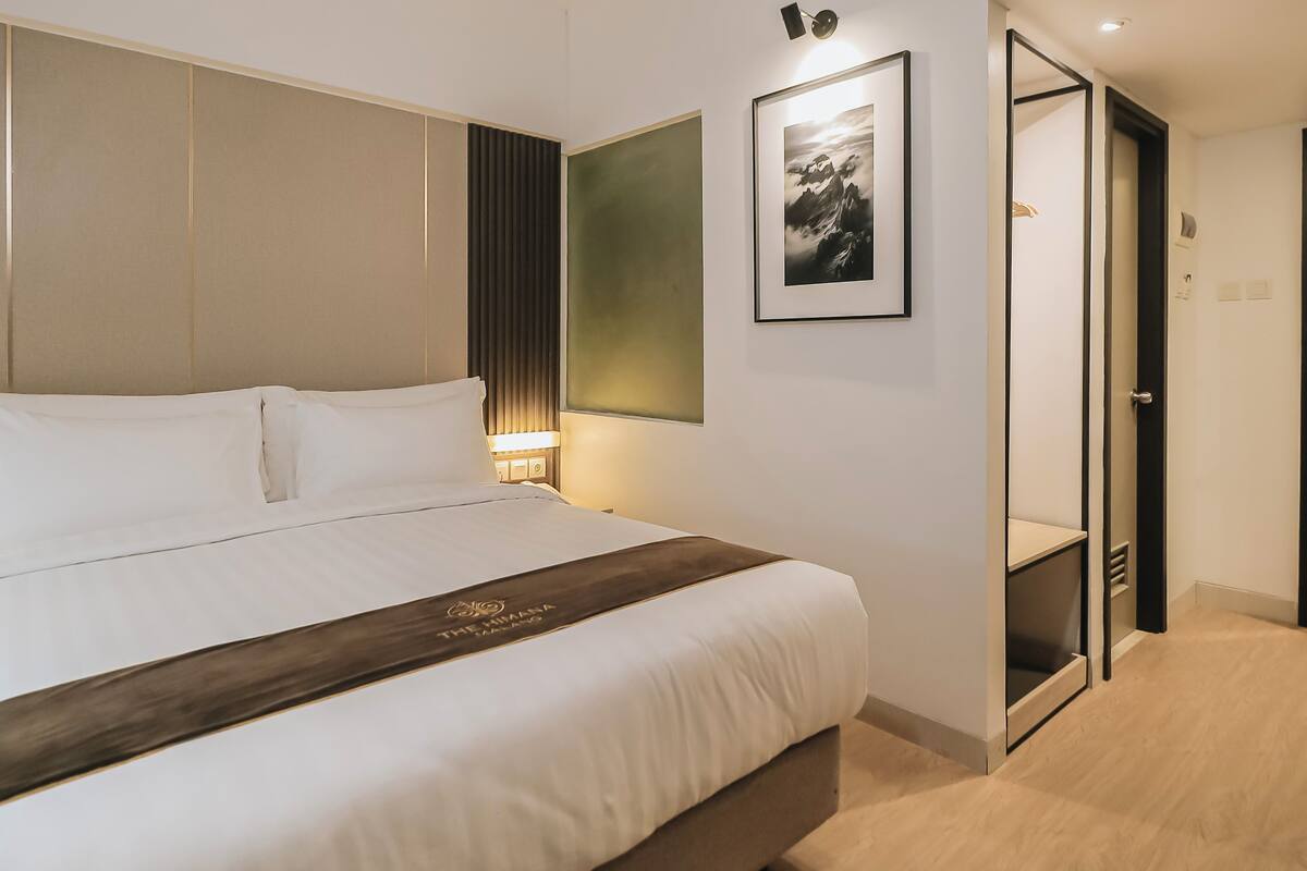 Une chambre d’hôtel avec un grand lit, une table de chevet, une lampe fixée au mur, un tableau encadré et une armoire.