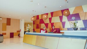 A reception desk with a geometric patterned wall, a potted plant, and a fire extinguisher. - The Himana Hotel Malang (Malang)