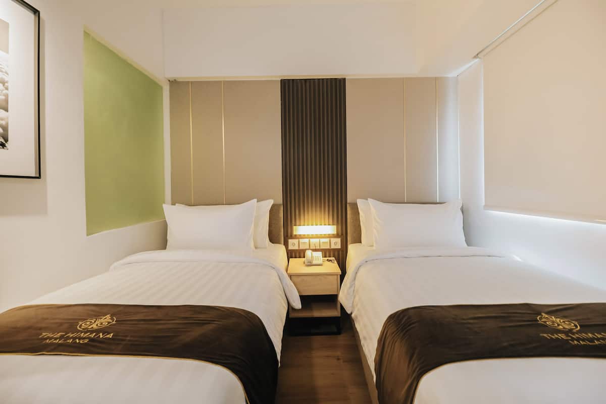 Une chambre d’hôtel avec deux lits, une table de chevet avec une lampe et un tableau encadré au mur.
