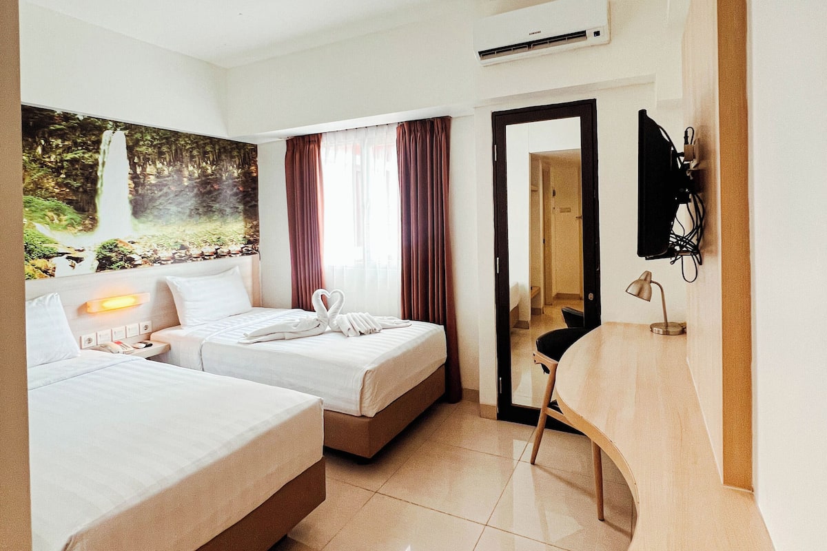 Une chambre d’hôtel avec deux lits, un bureau, une chaise, une télévision et un appareil de climatisation.