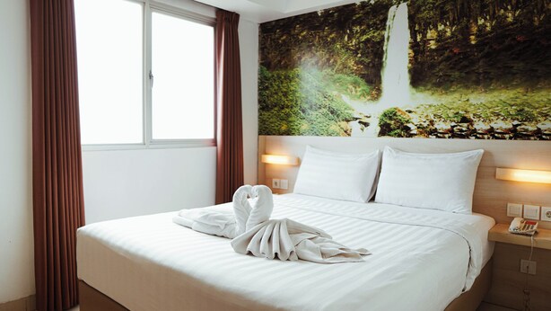 A hotel room with a bed, a painting of a waterfall, and a telephone on the nightstand. - The Himana Hotel Malang (Malang)
