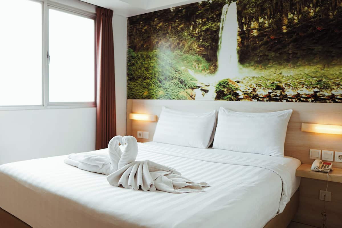 Une chambre d’hôtel avec un lit, un tableau représentant une cascade et un téléphone sur la table de chevet.