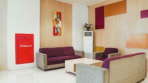 Een moderne hotelentree met een rode hydrant, paarse banken, een witte bijzettafel en een groot abstract schilderij aan de muur.