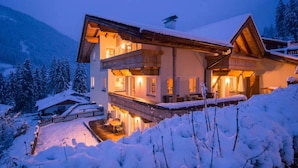 Een chalet met twee verdiepingen en een balkon, gelegen in een besneeerd landschap met bergen.
