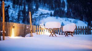 Een houten hek, een met sneeuw bedekte stoel en een met sneeuw bedekte tafel in een besneeuwde omgeving.