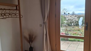 A room with a wooden floor, a hanging coat rack, a door leading to a garden, and a small vase with dried plants. - Cozy vacation apartment 70sqm for max. 4 persons with terrace (Laufen)