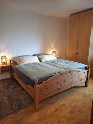 A wooden bed with a headboard, two bedside tables with lamps, a large wardrobe, and a carpeted floor.