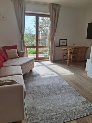 A room with a sofa, a desk, and a view through a large window.