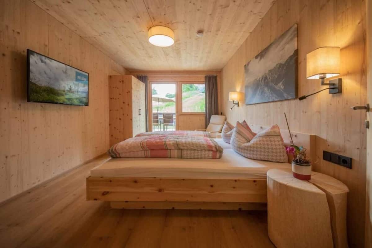 A wooden cabin bedroom with a bed, wall-mounted lamps, and a painting.