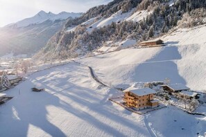 Een berglandschap bedekt met sneeuw, met een chalet omringd door bomen en een heldere lucht.