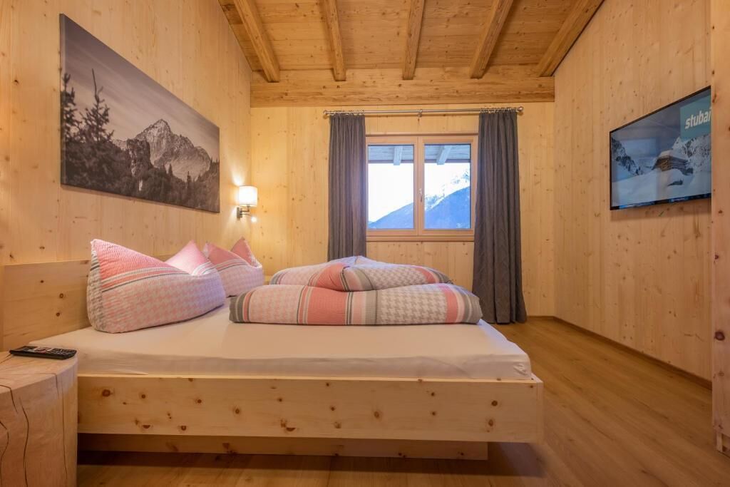 A wooden room with a bed, a TV, a painting, and a window with curtains.