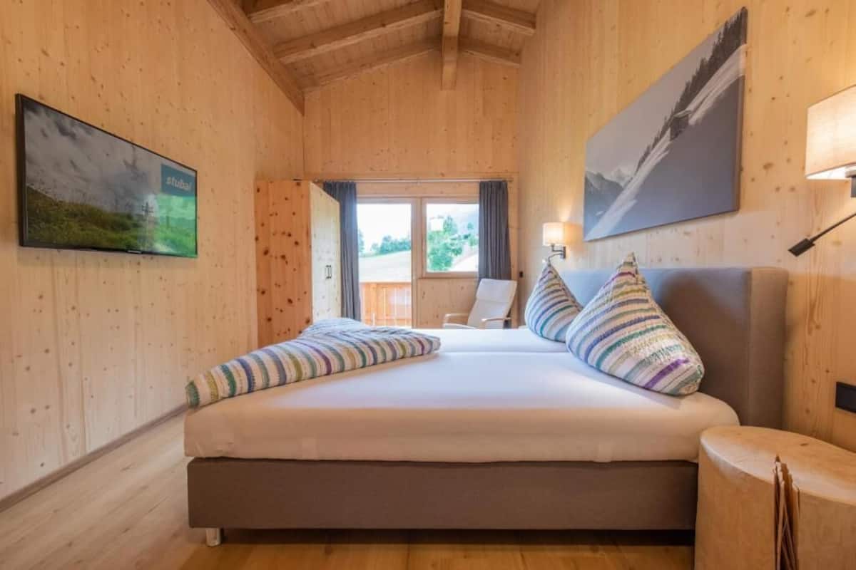 A wooden-paneled room with a bed, a chair, a TV, and a painting.
