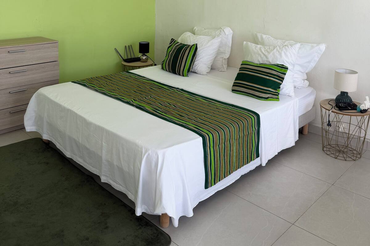 A neatly arranged bedroom with a bed, bedside table, lamp, and a decorative wall piece.