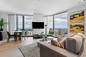 Ein modernes Wohnzimmer mit Essbereich, großen Fenstern, einem Flachbildfernseher und Blick auf die Stadt.