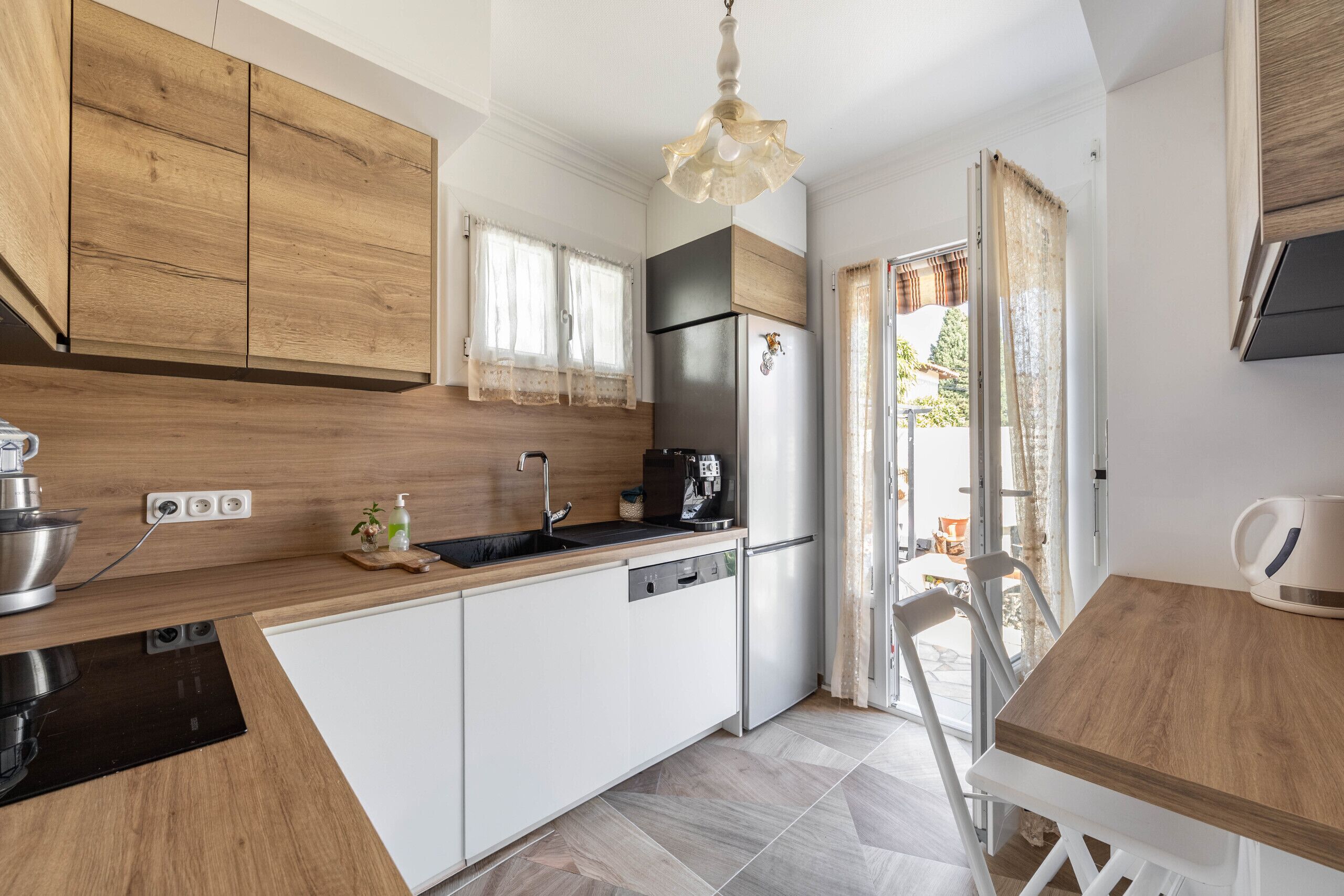A modern kitchen with wooden cabinets, a stainless steel refrigerator, a coffee machine, and a dining area with a table and chairs.. Happyfew Maison Eglantine