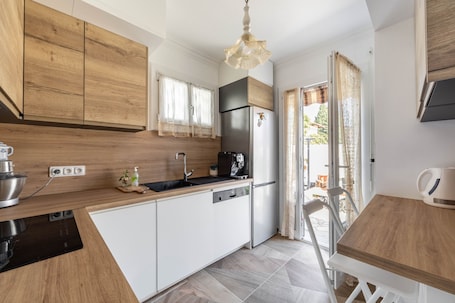 A modern kitchen with wooden cabinets, a stainless steel refrigerator, a coffee machine, and a dining area with a table and chairs.. Happyfew Maison Eglantine