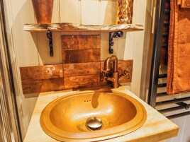 A bathroom with a wooden vanity, copper faucet, and a sink.